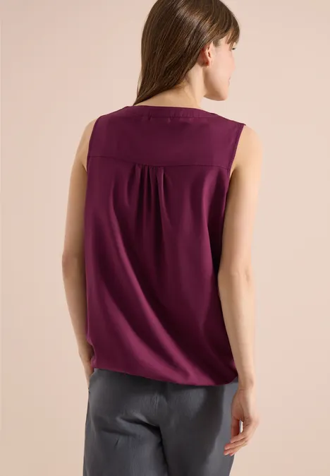 Femme de dos portant un haut sans manches violet et un pantalon gris sur fond clair.