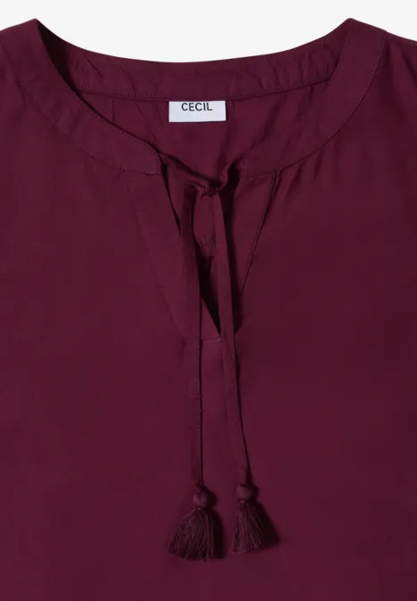 Blouse femme bordeaux à col rond avec liens à pompons décoratifs.