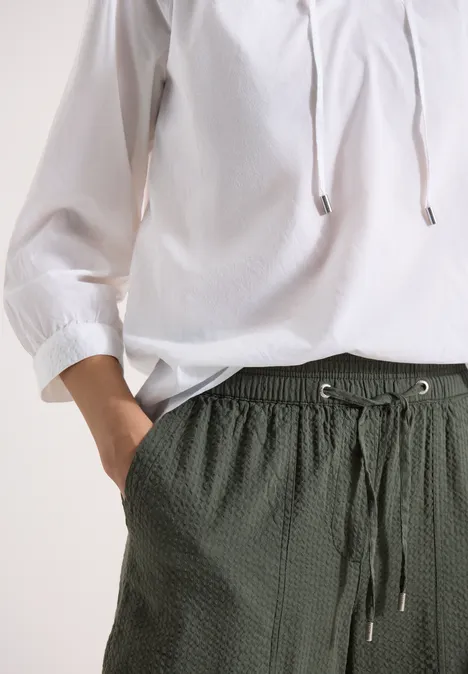 Weiße Bluse mit 3/4-Ärmeln und dunkelgrüner, strukturierter Hose mit Tunnelzug und Taschen.