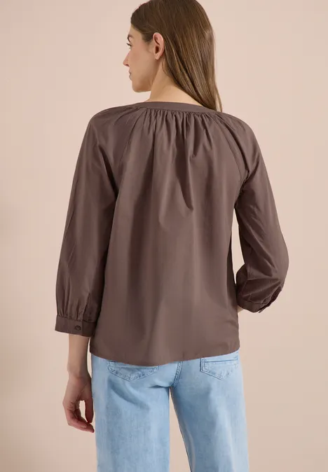Frau von hinten in brauner Bluse mit gerafftem Ausschnitt und hellblauen Jeans.