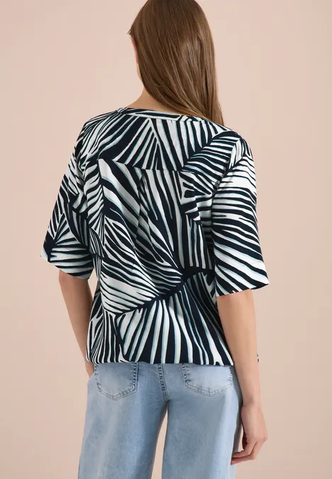 Frau trägt schwarz-weiße Zebramusterbluse mit Rückenknoten und blauen Jeans.