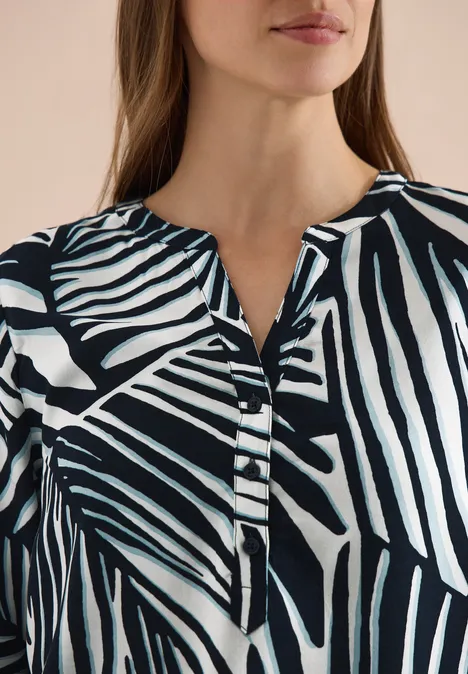 Obere Körperhälfte einer Frau in einer schwarz-weißen Bluse mit abstraktem Zebrastreifenmuster.