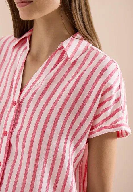 Frau mit rosa-weiß gestreiftem Hemd, nur Oberkörper sichtbar.