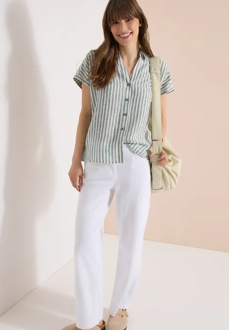 Une personne porte une chemise verte à rayures, un pantalon blanc et un sac à main.