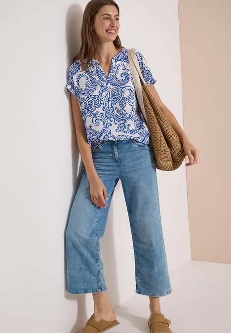 Blouse met split in de hals en print vanilla white Frau trägt blau-weiß gemusterte Bluse, weite Jeans, Nude-Pumps und geflochtene Tasche.