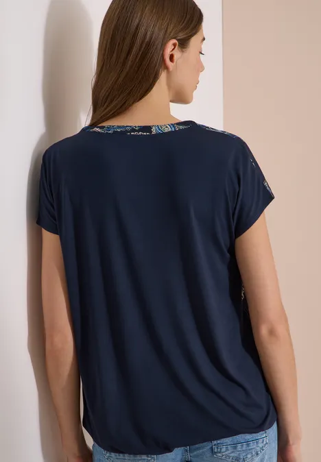 Blouse met split in de hals en een mix van texturen universal blue Frau von hinten trägt dunkelblaues T-Shirt mit kurzen Ärmeln vor heller Wand.