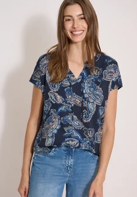 Blouse met split in de hals en een mix van texturen universal blue Junge Frau vor neutralem Hintergrund, trägt blaues T-Shirt mit Paisley-Muster und blaue Jeans.
