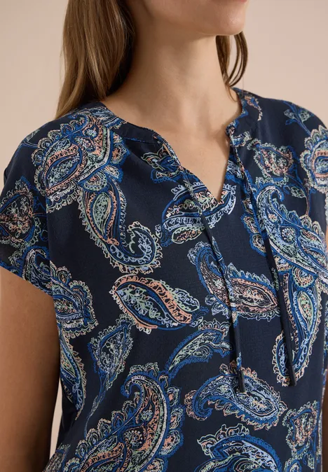 Blouse met split in de hals en een mix van texturen universal blue Damenbluse mit kurzärmeligem Schnitt und blau-orangem Paisley-Print auf dunklem Untergrund.