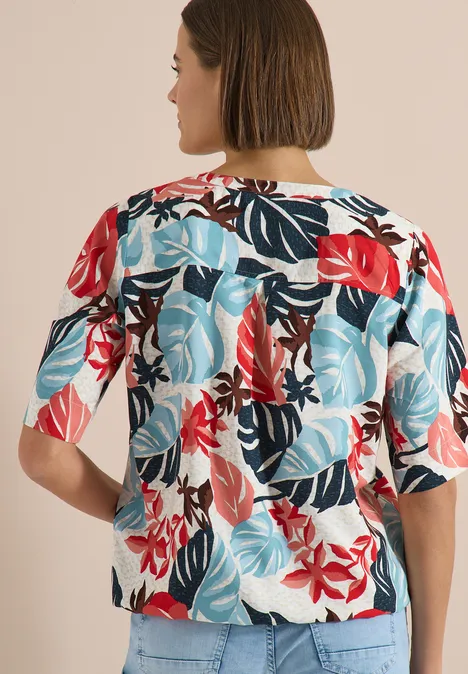 Kurzarm Bluse mit Split Neck light alabaster white Rückenansicht einer Frau mit Kurzhaarschnitt, die eine kurzärmelige Bluse mit rot-blauem tropischem Blatt- und Blumenmuster trägt.