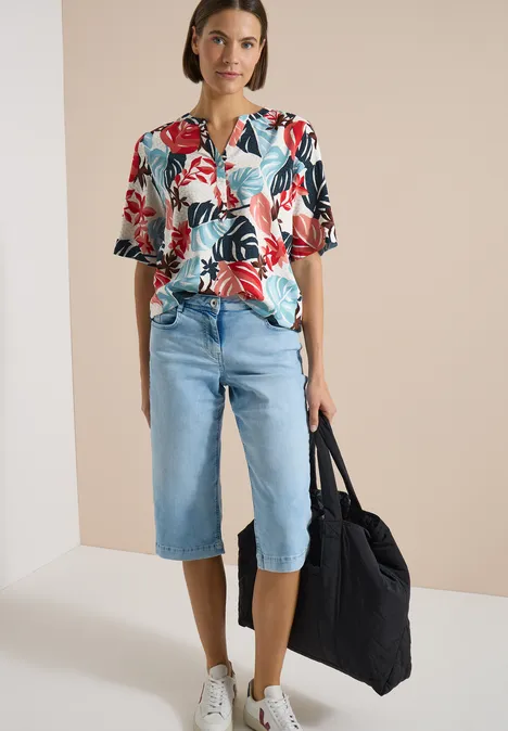 Kurzarm Bluse mit Split Neck light alabaster white Person trägt ein buntes Hemd mit Blumenmuster, knielange Jeans-Shorts und hält eine große schwarze Tasche.