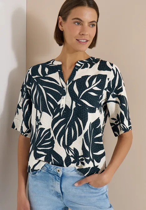 Blouse met korte mouwen en gespleten hals palm breeze green Frau trägt kurzärmlige Bluse mit blau-weißen Blattmustern vor neutralem Hintergrund.