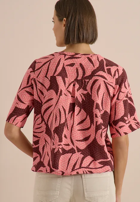 Blouse met korte mouwen en gespleten hals null Rückenansicht einer Person in locker geschnittenem pinkem Oberteil mit schwarzem Blattmuster und weißen Hosen.