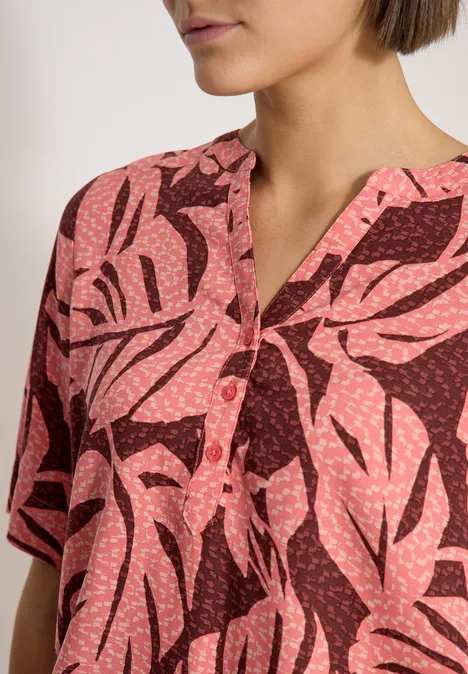 Blouse met korte mouwen en gespleten hals null Nahe Aufnahme eines kurzärmligen Oberteils mit rosa Blättermuster auf dunklem Grund.