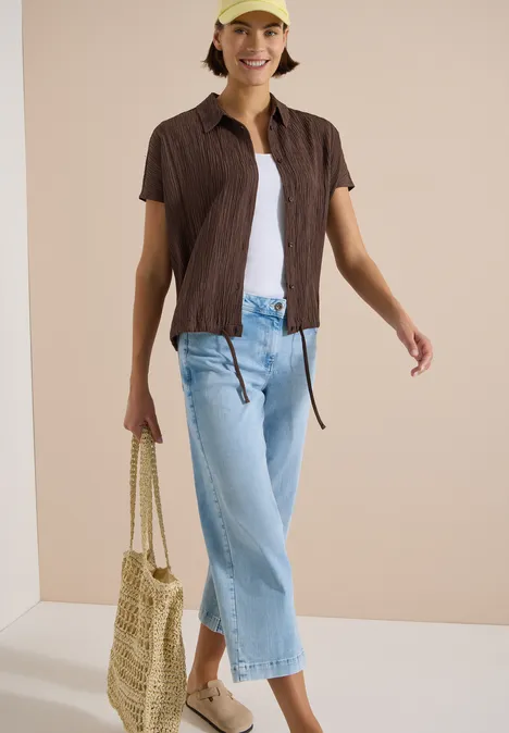 Dropped Shoulder Hemdbluse in Unifarbe brown cacao Frau trägt hellblaue Culotte-Jeans, weißes Top, braunes Kurzarmhemd und geflochtene Tasche.