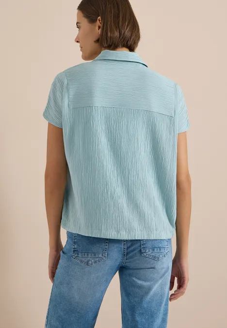 Dropped Shoulder Hemdbluse in Unifarbe crystal mint Eine Person von hinten trägt eine hellblaue kurzärmelige Bluse und Jeans vor beigem Hintergrund.