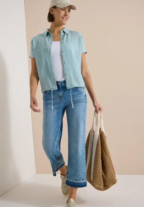 Dropped Shoulder Hemdbluse in Unifarbe crystal mint Frau in sommerlicher Freizeitkleidung: grünes Hemd, weißes Top, weite Jeans, Strohtasche und Sandalen.