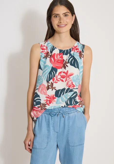 Blouse met ronde hals en bladerenprint light alabaster white Vrouw draagt mouwloze, kleurrijke bloementop en blauwe broek, staat met handen in de zakken.