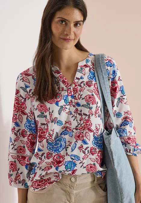 Vrouw draagt witte blouse met rode en blauwe bloemen, 3/4-mouwen, met blauwe denim tas.