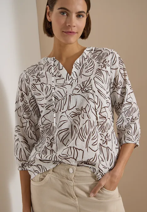3/4-Arm Tunika mit Blätterprint light alabaster white Person trägt weiße Bluse mit braunem Blattmuster und helle Hose, eine Hand in der Tasche.