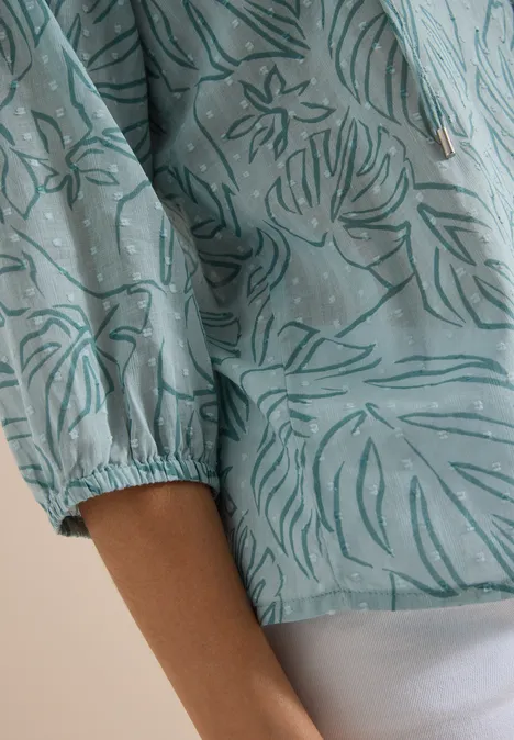 3/4-Arm Tunika mit Blätterprint crystal mint Nahaufnahme einer Person mit türkiser Bluse mit Blumenmuster und weißer Hose.
