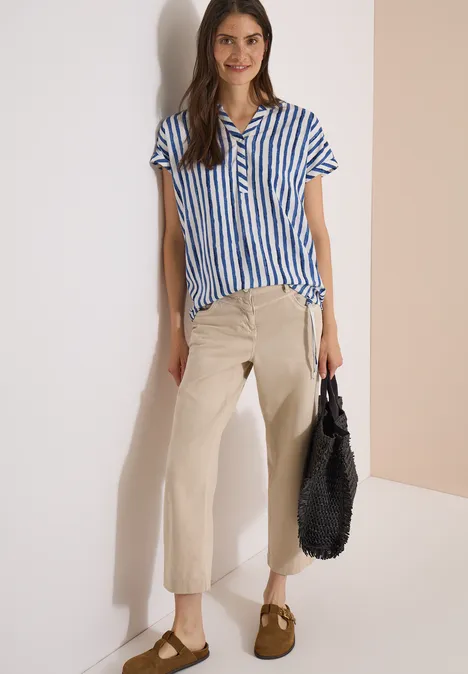 Dropped Shoulder Bluse mit Streifen urban navy blue Frau trägt blau-weiß gestreiftes Hemd, beige weite Hosen, braune Schuhe und hält eine schwarze Tasche.