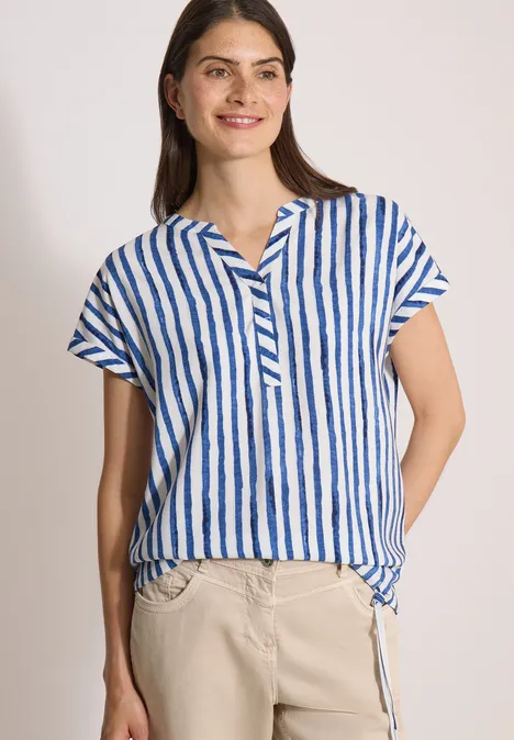 Dropped Shoulder Bluse mit Streifen urban navy blue Frau trägt blau-weiß gestreiftes Kurzarmhemd und helle Hose vor neutralem Hintergrund.