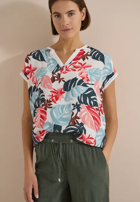 Bluse mit Split Neck und Printmix light alabaster white Person trägt bunte, floral gemusterte Bluse mit V-Ausschnitt und dunkelgrüner Hose mit Taschen.