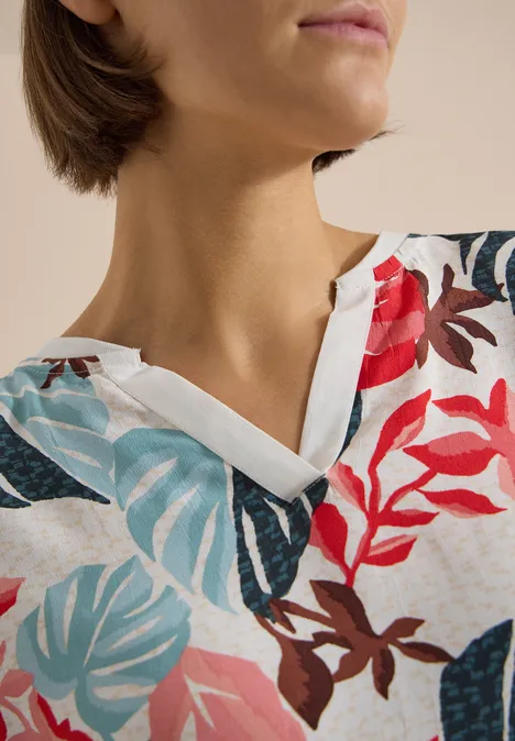 Bluse mit Split Neck und Printmix light alabaster white Frau in weißer Bluse mit buntem Blattmuster (Rot, Blau, Grün) und V-Ausschnitt.