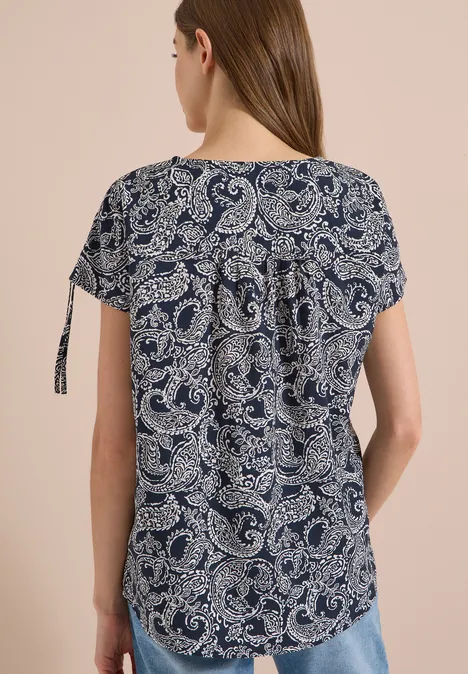 Haut féminin bleu foncé à motifs paisley blancs, manches courtes avec liens latéraux.