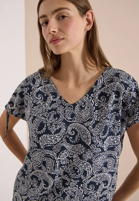 Femme portant un chemisier bleu foncé à motif paisley et col en V, sur fond neutre.