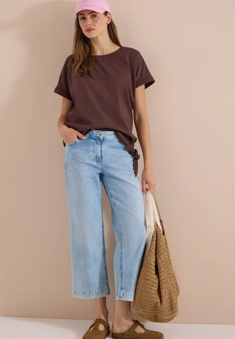 Blouse met ronde hals en knoopdetail brown cacao Frau trägt braunes T-Shirt, weite helle Jeans und hält eine große geflochtene Tasche.