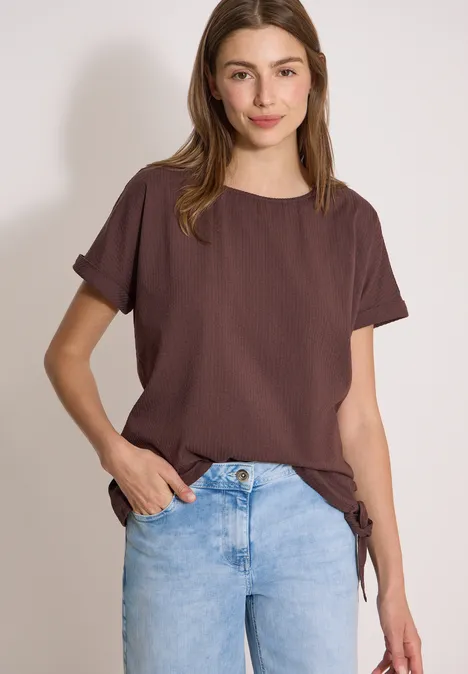 Blouse met ronde hals en knoopdetail brown cacao Frau trägt braunes T-Shirt und helle Jeans vor neutralem Hintergrund.