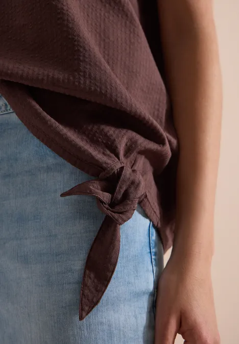 Blouse met ronde hals en knoopdetail brown cacao Nahaufnahme eines braunen, seitlich geknoteten Oberteils mit Jeans und sichtbarem Arm.