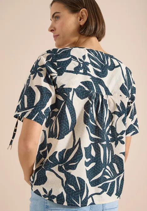 Bluse mit Rundhals und Raffung palm breeze green Frau trägt weiße Bluse mit dunkelblauem Blattmuster, halblange Ärmel und seitliche Bändchen.