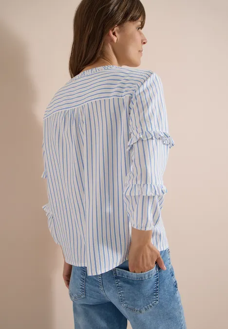 Frau von hinten in blau-weiß gestreifter Bluse mit Rüschenärmeln und Jeans.