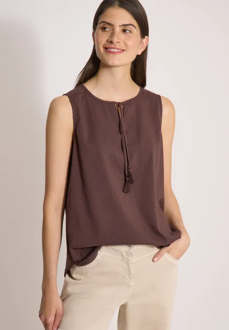 Blusentop mit Split Neck und Bändern brown cacao Eine Frau trägt eine ärmellose braune Bluse und beige Hosen und posiert lässig mit einer Hand in der Tasche.