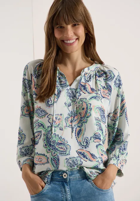 Een vrouw draagt een losse blouse met kleurrijk paisley-patroon en V-hals.