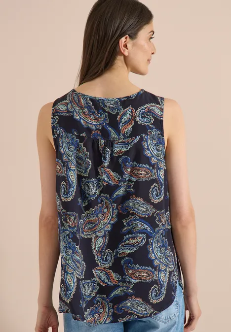 Haut chemisier à col fendu et imprimé universal blue Vue de dos d’une femme en top sans manches à col rond et motif cachemire multicolore sur fond sombre.