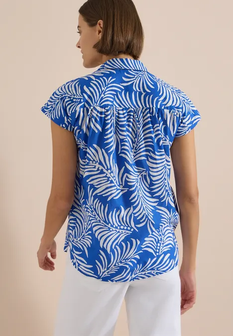 Kurzarm Hemdbluse mit Print surf blue Eine Frau steht von hinten, trägt ein blaues Hemd mit weißen Blattmustern und eine weiße Hose.