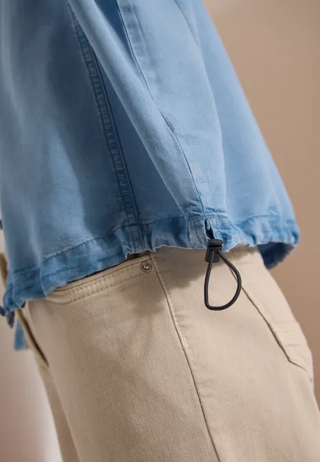 Seitliche Ansicht eines Teils einer Person in beiger Hose und blauem Oberteil mit Kordelzug am Saum.