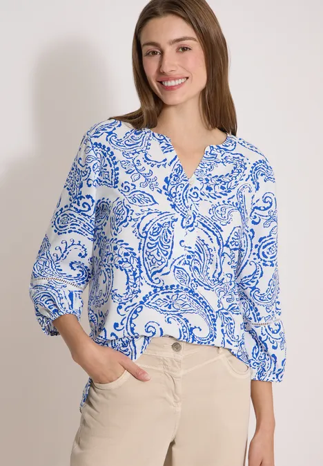 Tuniek met 3/4-mouwen en print vanilla white Frau in weißer Bluse mit blauem Paisley-Muster und beiger Hose vor schlichter Kulisse.