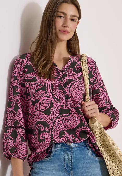 Femme portant un chemisier à motifs roses, jean et sac en osier.