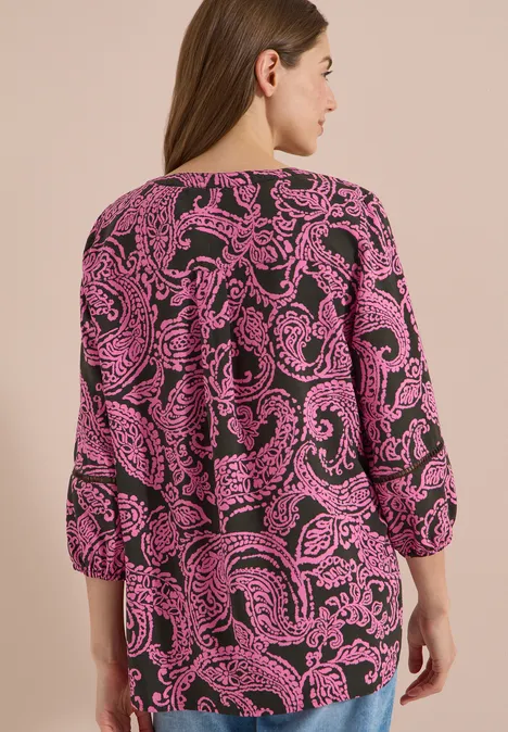 Femme de dos portant une blouse à motif cachemire rose et noir.