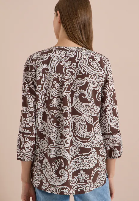 Femme vue de dos en blouse marron à motif cachemire blanc.