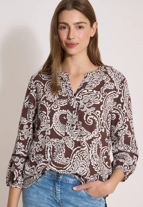 Femme portant un chemisier marron à motif cachemire et jean bleu.
