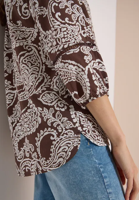 Vue de côté d’un haut marron à motifs paisley blancs porté avec un jean bleu.