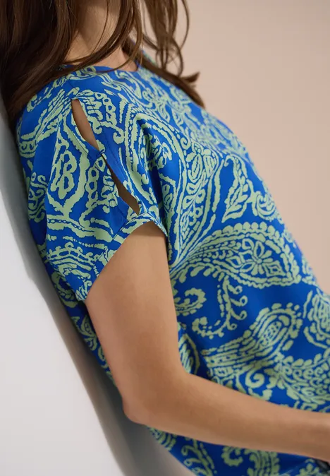 Seitliche Ansicht einer Person in blauem Shirt mit grünem Paisley-Muster.
