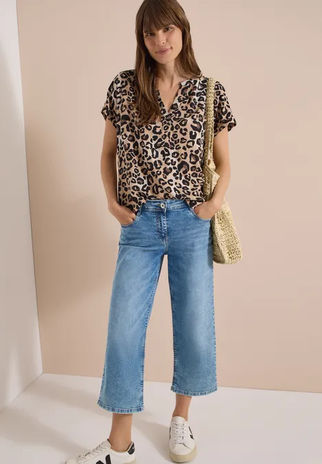 Kurzarm Bluse mit Split Neck und Leo-Print urban taupe Frau mit Leopardenbluse, weiten Jeans-Culottes, weißen Sneakern und Strohtasche vor beiger Wand.