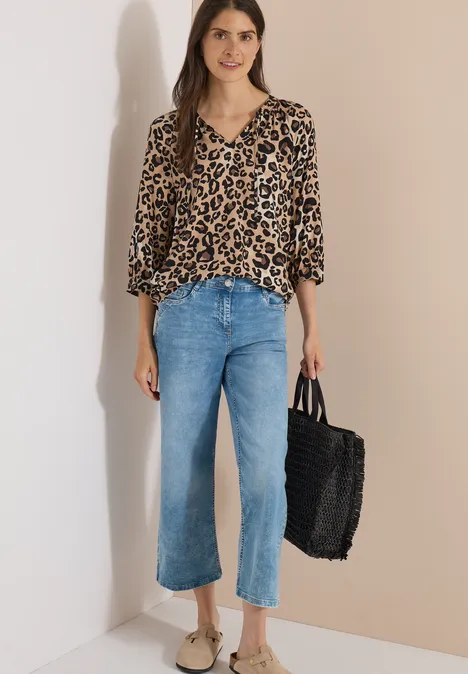 Tunique à manches 3/4, à col fendu et imprimé urban taupe Femme portant une blouse léopard ample, un jean bleu clair raccourci et un sac tressé noir.
