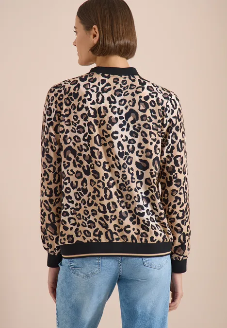 Vue de dos d'une personne portant une veste léopard à bords noirs et un jean bleu clair sur fond beige.